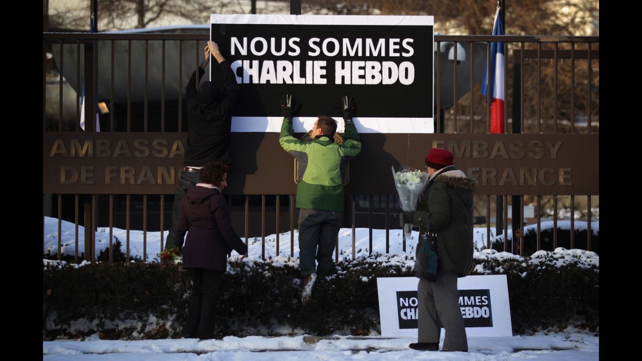 Employees put up a sign as a woman prepares to place a bouquet of flowers at the front gate of the French Embassy in Washington on January 7.