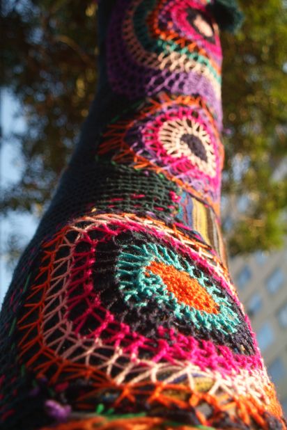 A yarn-bombed tree stands on a street in Barrio Bellavista.