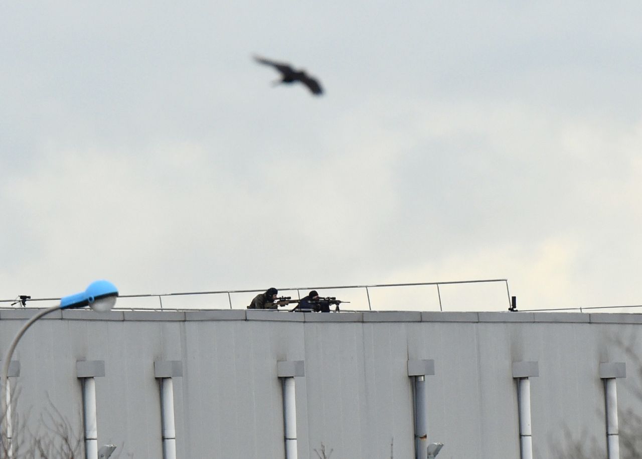 A bird flies overhead as police snipers take aim from a roof.