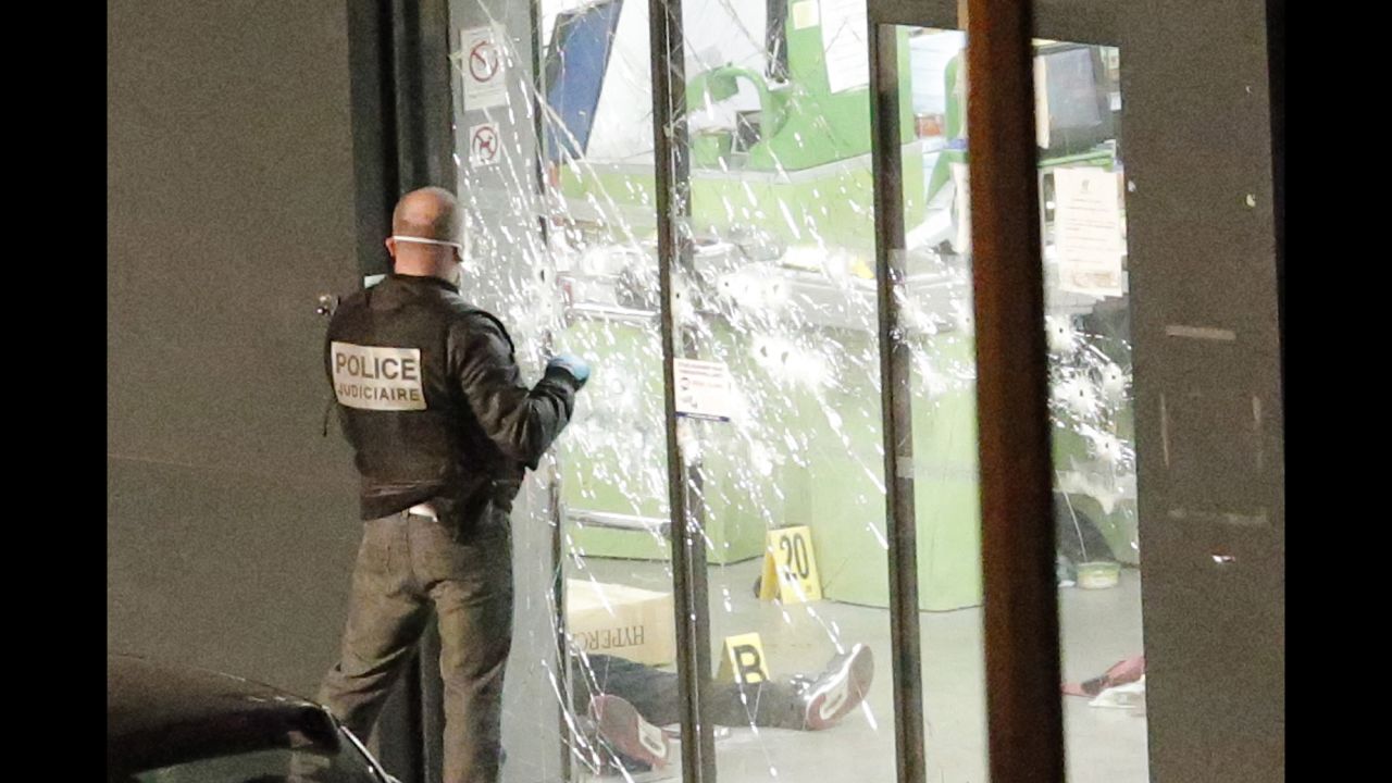 A police officer closes the bullet ridden door next to a body lying in a kosher grocery store in the Paris neighborhood of Porte de Vincennes on Friday, January 9. Amedy Coulibaly -- the man who authorities believe killed a policewoman Thursday south of Paris -- was killed when police stormed the store. A search is underway for suspected accomplice, a woman identified as Hayat Boumeddiene. <br />