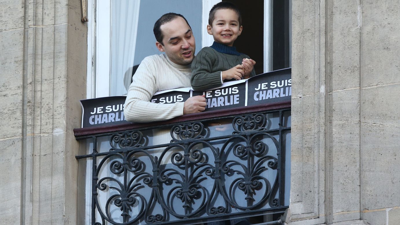 A man and boy watch people gather for the rally from a balcony near the Place de la Republique.