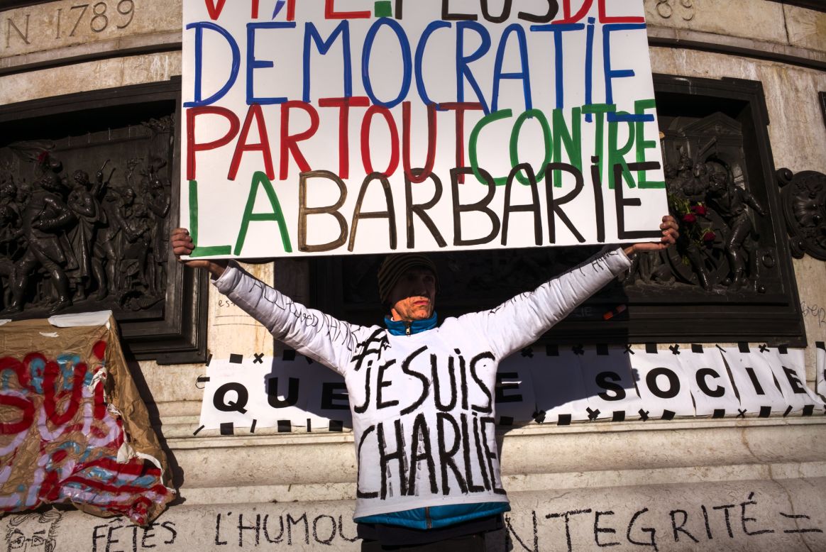 A demonstrator holds a sign that translates to "Urgent: More democracy everywhere against barbarism."