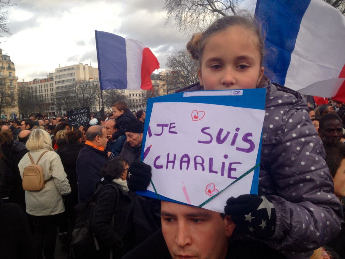 A little girl holds up a sign while sitting on the shoulders of a man at the Paris unity rally.