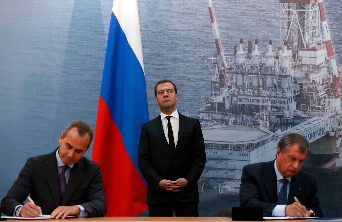 Russia's Prime Minister Dmitry Medvedev (C) stands in front of the huge photo of a fixed offshore ice-resistant platform of the oil giant Lukoil during a signing ceremony between Russia's Rosneft oil company and Sweden's Lundin Petroleum in the Russian Caspian Sea port of Astrakhan, on October 2, 2013