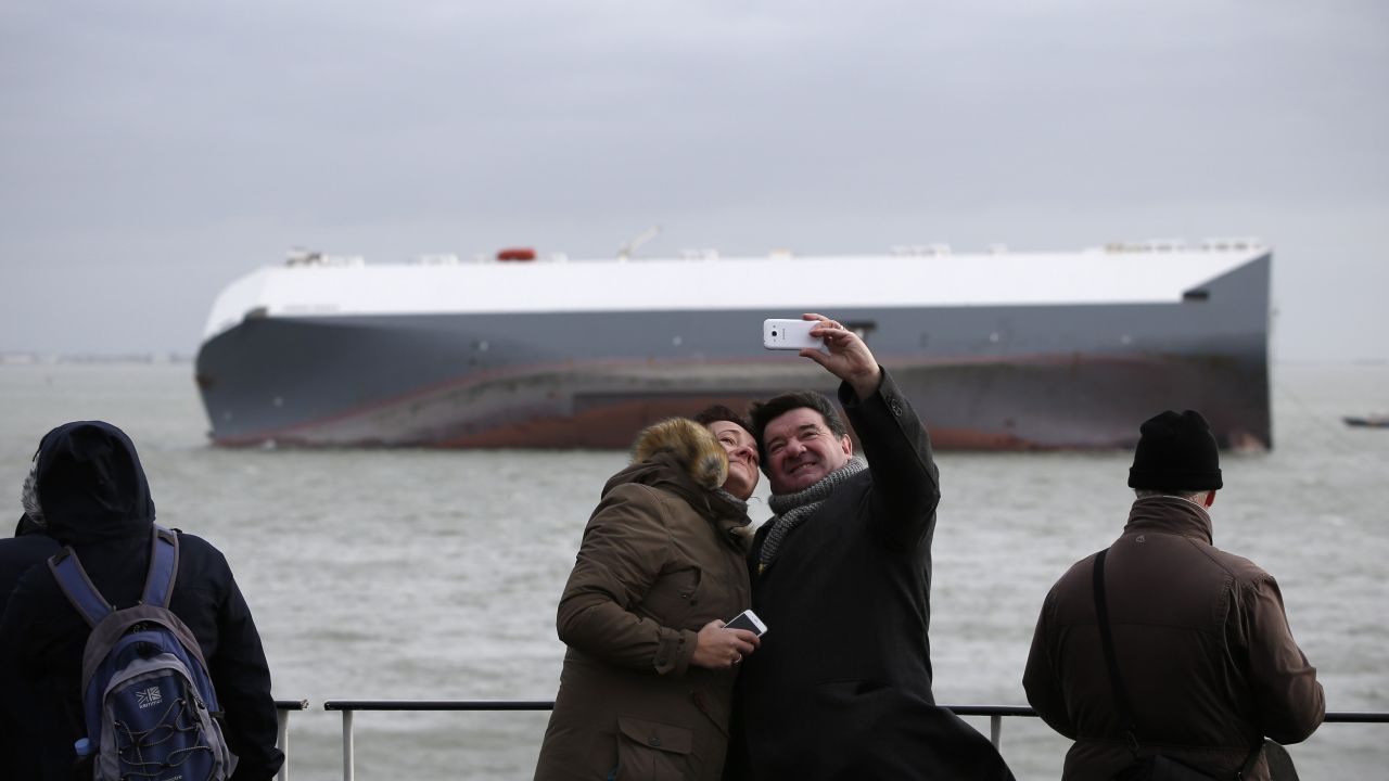 Ferry passengers take a photo together as they pass the grounded Hoegh Osaka cargo ship on Wednesday, January 7. The cargo ship ran aground in the Solent, a strait near southern England, several days earlier. 