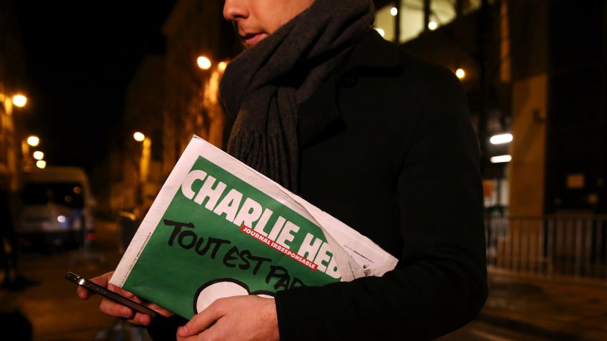 PARIS, FRANCE - JANUARY 13: A journalist holds an early copy of a Charlie Hebdo magazine while delivering a news report outside the offices of Liberation Newspaper Group on January 13, 2015 in Paris, France. Three million copies of the controversial magazine have been printed and are due to be released tomorrow, in the wake of last weeks terrorist attacks. (Photo by Dan Kitwood/Getty Images)