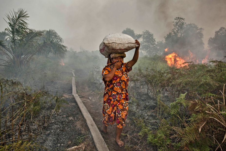 A woman walks through haze as a forest fire burns bushes and fields, June 27, 2013 in Riau province, Indonesia. The fires on Sumatra caused record smog levels in Malaysia and Singapore. Sumatra was forced to step up efforts to fight the fires to relieve conditions, with eight farmers arrested for starting the fires.