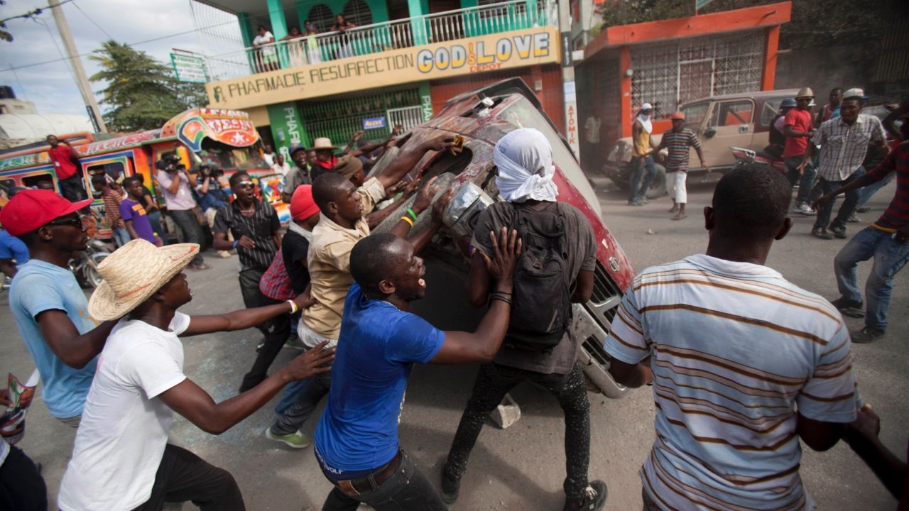 People in Port-au-Prince, Haiti, flip over a car to block a street during a protest demanding the resignation of President Michel Martelly on Sunday, January 11.