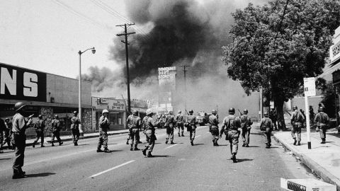 Armed National Guardsmen march toward smoke on the horizon during the street fires of the Watts riots, Los Angeles, August 1965. 