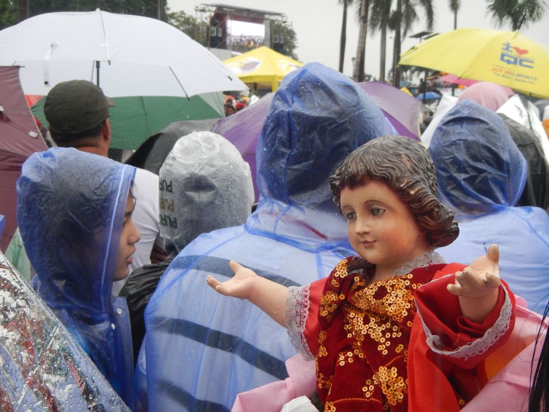 As the crowds watch the Mass on a giant video screen, a "Santo Nino" reaches out to greet passersby.