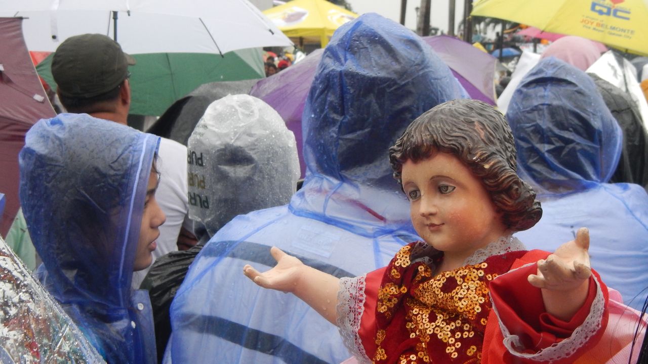 As the crowds watch the Mass on a giant video screen, a "Santo Nino" reaches out to greet passersby.