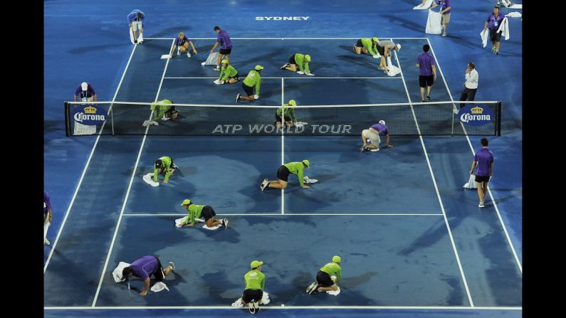 Staff members and ball kids try to dry a tennis court before a first-round match at the Sydney International on Tuesday, January 13.