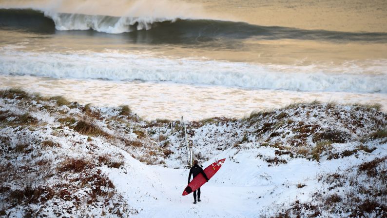 Pro surfer Alastair Mennie walks through snow as he makes his way toward the beach in Portrush, Northern Ireland, on Wednesday, January 14.