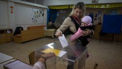 A woman carrying a baby casts her vote in the Greek general election at a polling station in a school in a suburb of Athens on January 25, 2015.