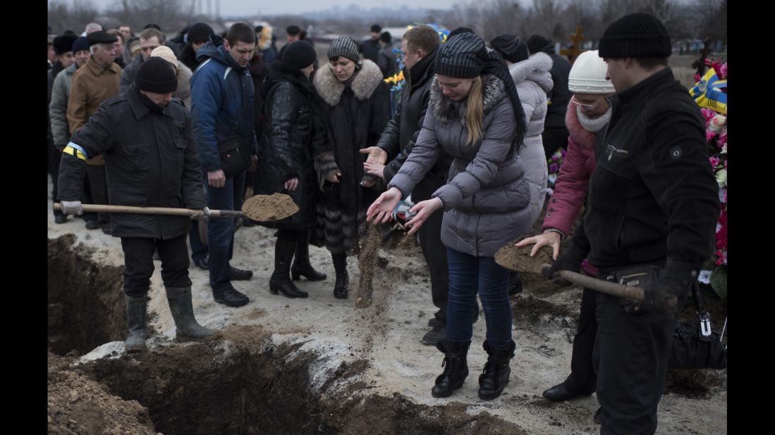 People in Mariupol, Ukraine, pour soil into the grave of a recent shelling victim on Monday, January 26. 