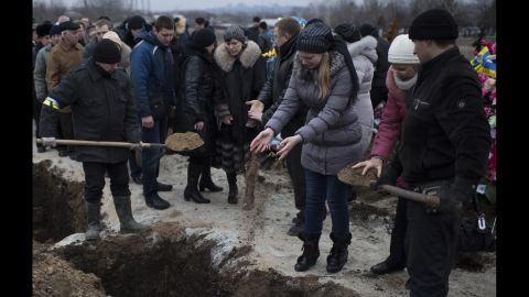People in Mariupol, Ukraine, pour soil into the grave of a recent shelling victim on Monday, January 26. 