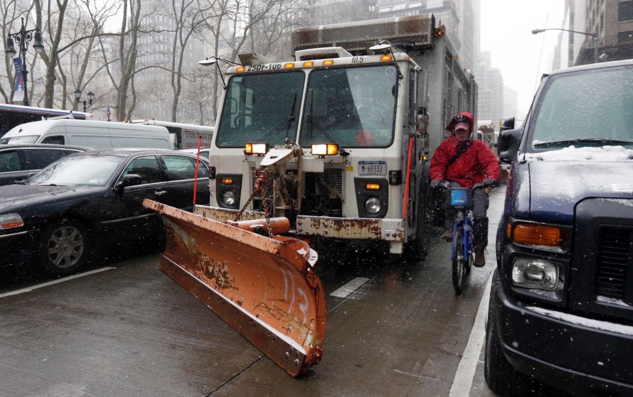 A cyclist in New York navigates between parked cars and a sanitation truck with a snow plow on it on January 26.