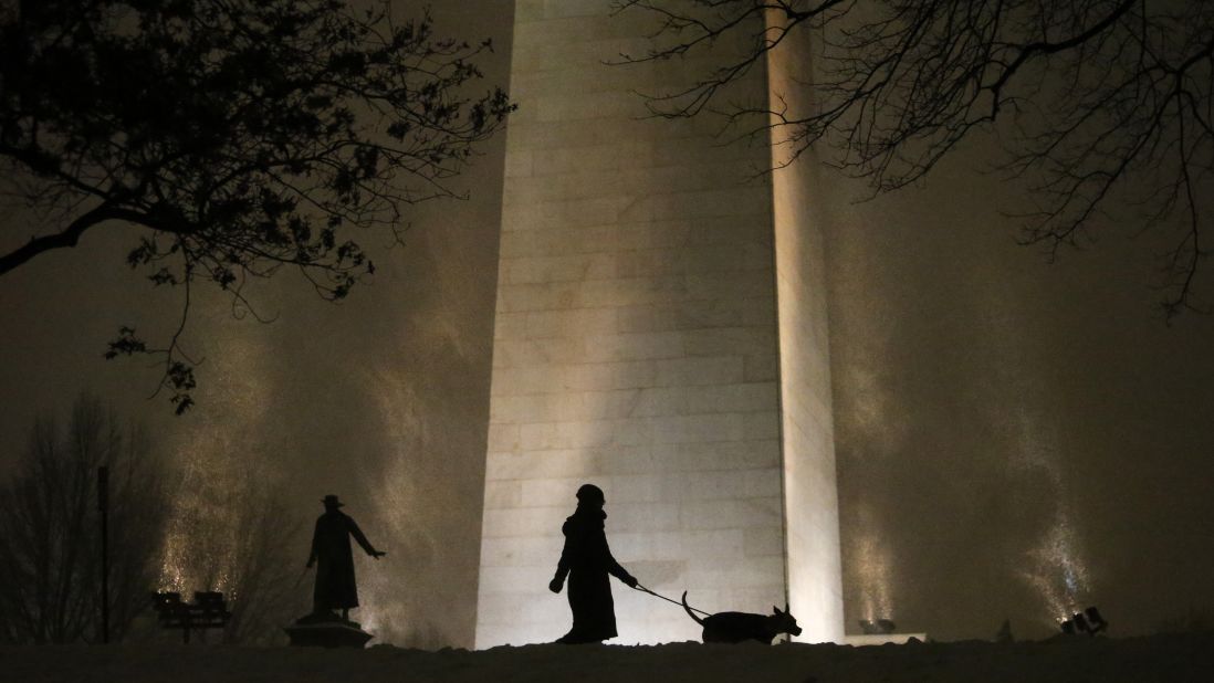 A woman walks her dog as snow swirls around the Bunker Hill Monument in Boston on Monday, January 26. 