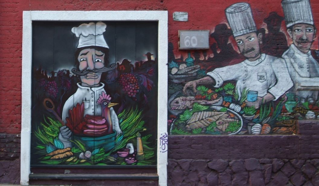 In front of a private parking lot for diners opposite, a mural of cooks in a kitchen add humor to an otherwise plain area.
