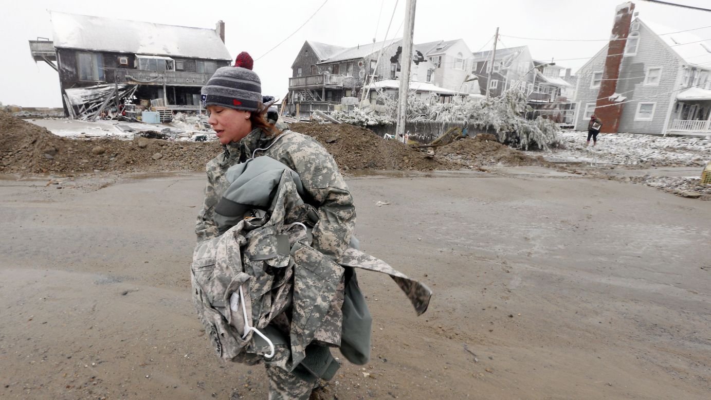 U.S. Army soldier Jennifer Bruno carries belongings from her house, center rear, which was heavily damaged by storm surge in Marshfield, Massachusetts.