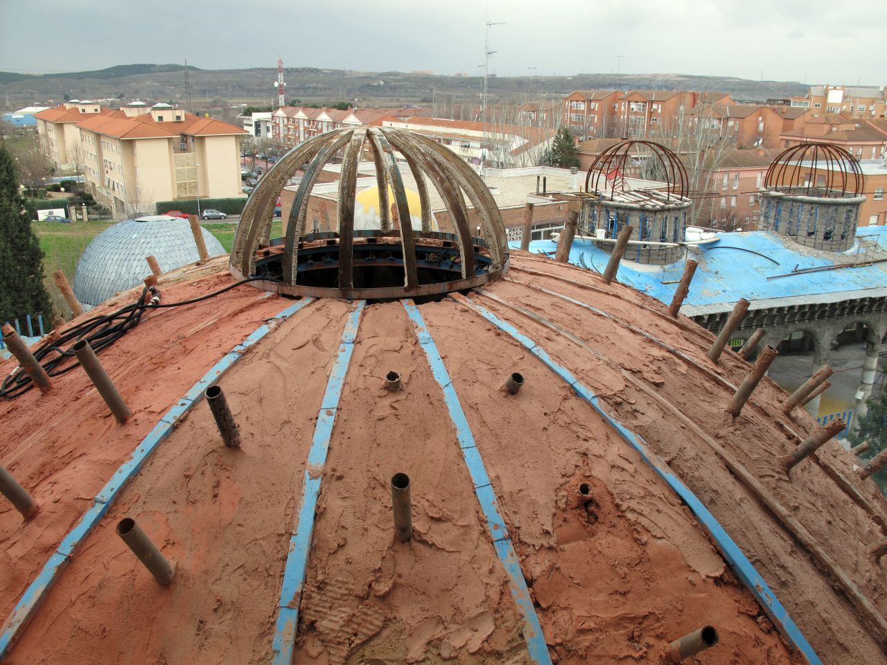 Small domes on the roof of the cathedral are pictured with the the residential buildings of Mejorada del Campo in the background. The largest dome is similar in appearance to the famous St Peter's basilica in the Vatican City.