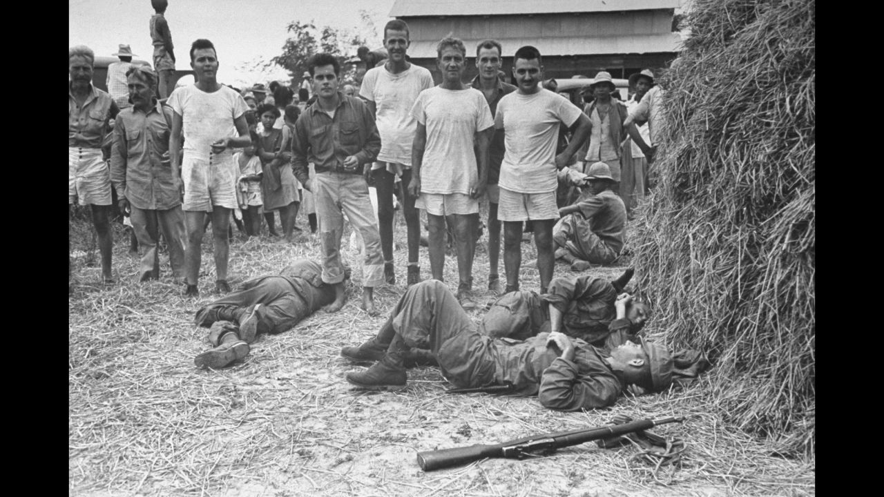 Exhausted Army Rangers sleep on straw-covered ground in front of some of the POWs they rescued.