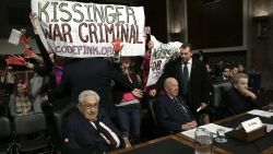 WASHINGTON, DC - JANUARY 29: Protesters shout "Arrest Henry Kissinger for war crimes" as (L-R) Former U.S. Secretary of State Henry Kissinger; former U.S. Secretary of State George Shultz and and former U.S. Secretary of State Madeleine Albright wait to testify before the Senate Armed Services Committee January 29, 2015 in Washington, DC. The committee heard testimony from Kissinger, Schultz and Albright on the topic of global challenges and U.S. national security strategy.