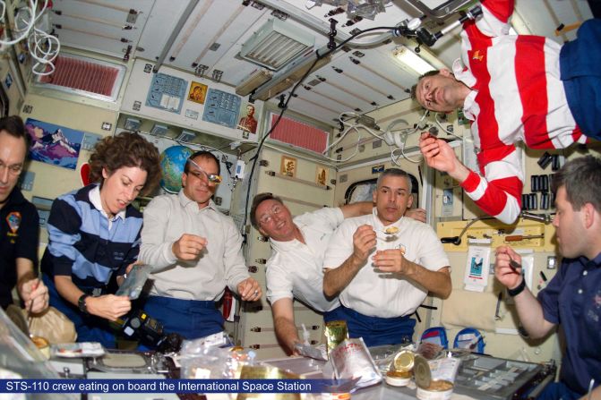 Astronautas flotando a la hora de la comida.   En la Estación Espacial Internacional los astronautas comen en una mesa plegable, asegurando los alimentos con velcro o cordones elásticos. Pero, ¿qué es lo que realmente comen?   