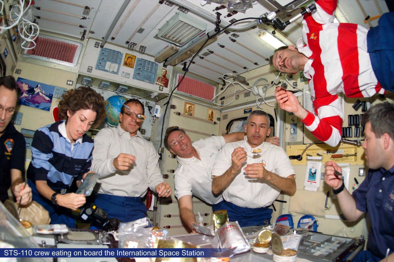 Astronauts floating around at meal time. On the International Space Station astronauts eat at a fold-down table, with food items secured with Velcro or bungee cords. But what do they actually eat?   