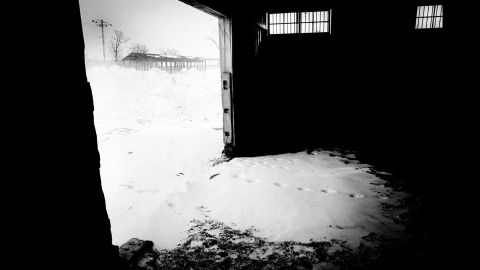Horse tracks are seen on snow inside an empty stable.