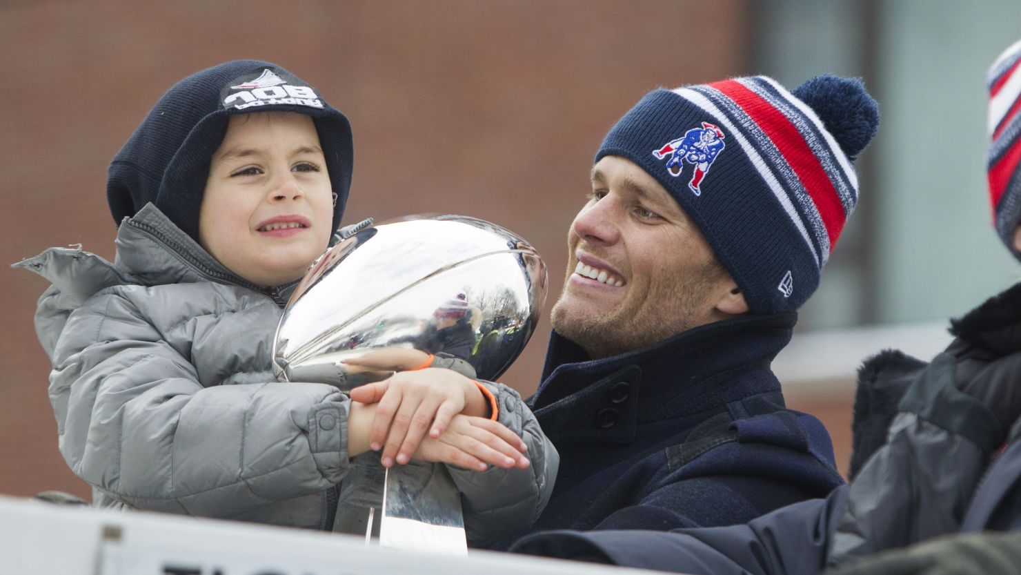 Benjamin Brady, left, holds the Lombardi trophy next to his dad, Patriots quarterback Tom Brady, on a duck boat during the New England Patriots victory parade February 4 in Boston.