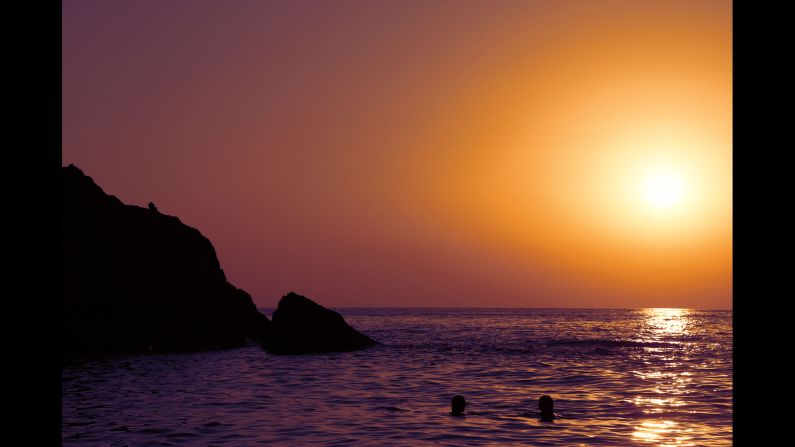 Two swimmers enjoy a sunset over Artemis' Cove.