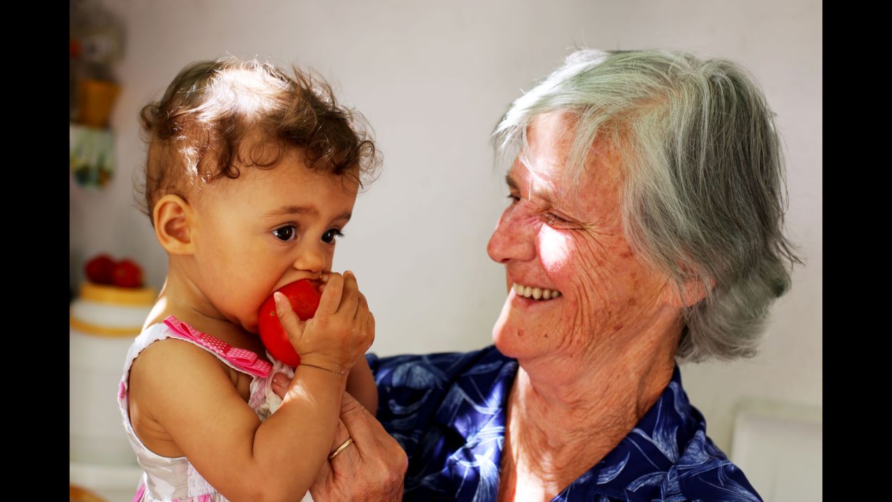 Antiiopi Koufadakis, an 80-year-old cancer survivor, feeds a homegrown tomato to her granddaughter. Her father lived to 98.