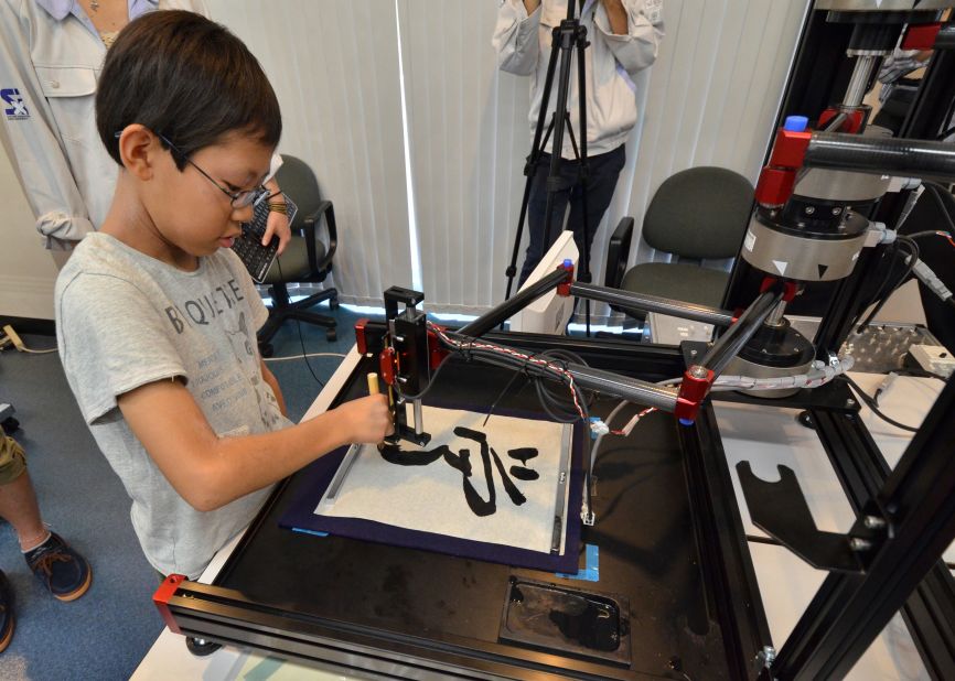 A boy writes a Chinese letter for 'study' with a calligraphy robot, which mimics the exact brush strokes of a master calligrapher, at a science workshop for elemenatry children at Keio University in Yokohama, suburban Tokyo on July 30, 2013. The motion copy robot, developed by Japan's Keio University associate professor Seiichiro Katsura, can recreate master works and the users can experience the same pressure and the same gestures of brush works by master painters or calligraphers.