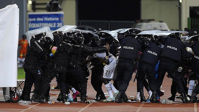 Police officers protect footballers from missiles thrown by fans.