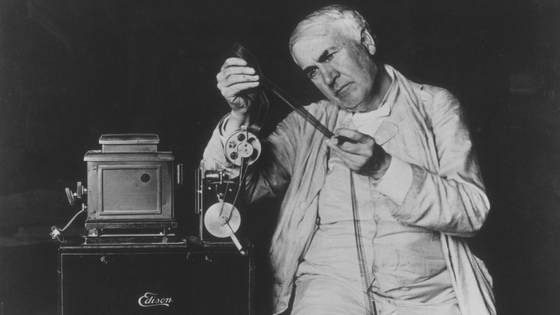 Thomas Edison examining motion picture film threaded through one of his film projectors.  
