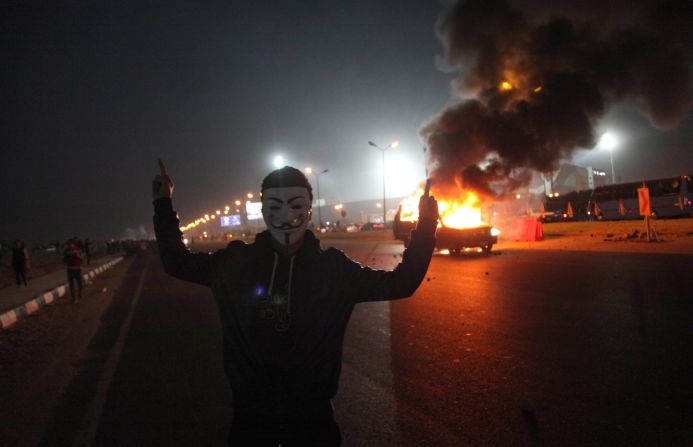 A masked man gestures near a burning car outside the stadium. 