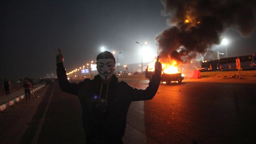 A masked man gestures near a burning car outside a sports stadium in Cairo's northeast district during clashes between supporters of Zamalek FC and security forces. 