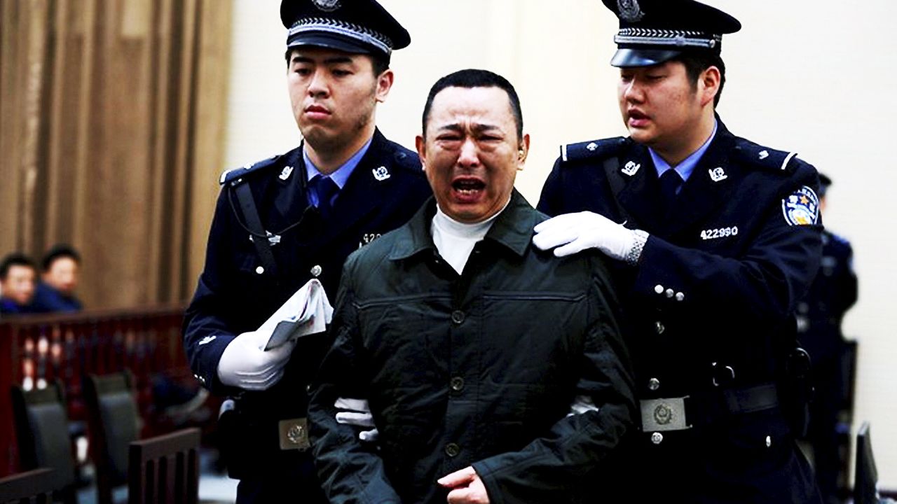 Liu Han, center, cries as he is escorted by police officers during his trial on 16 April 2014. 