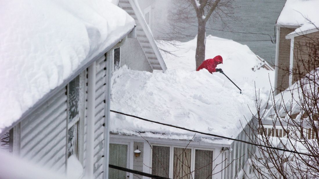 A man climbs onto his roof to clear piles of snow in Quincy, Massachusetts, on February 9.