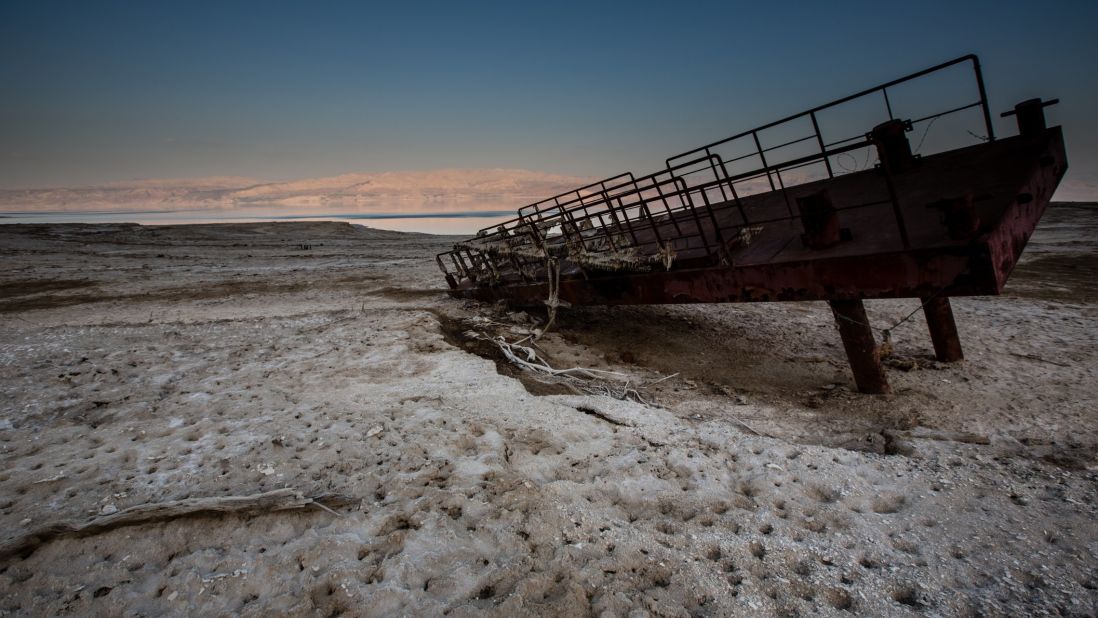 A rusty old dock lies atop a desert encrusted in salt. What used to be the shoreline of the Dead Sea now lies hundreds of feet from the water's edge.