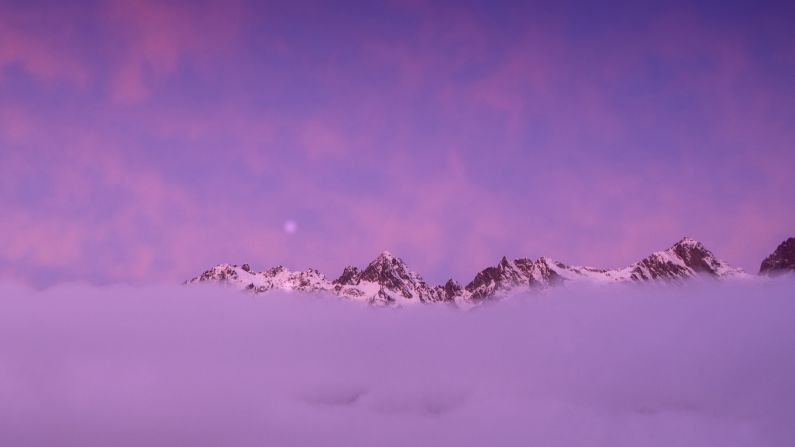 Clouds high up in the Alps appear pink in the glow of sunrise.
