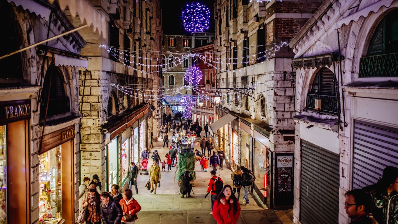 Tourists and holiday shoppers browse the alleyway storefronts near the Rialto Bridge.