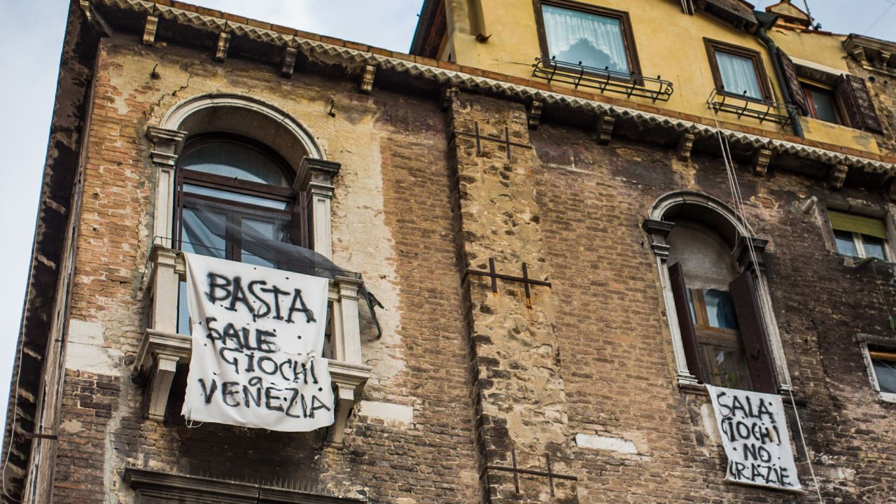 An anti-Mafia banner, reading "Enough - out of Venice" hangs from a Venetian window above the canals.