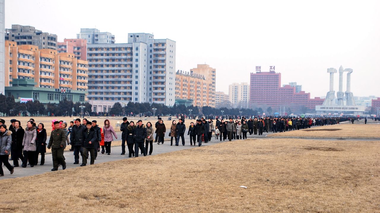 Citizens walk in orderly fashion to a show celebrating Kim Jong Il. The Korean Workers Party Monument, a Pyongyang landmark, is in the distance.