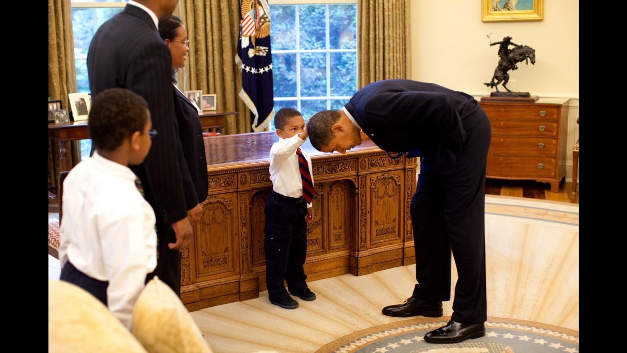 Obama bends over so the son of a White House staff member can pat his head during a visit to the Oval Office in May 2009. The boy wanted to know if Obama's hair felt like his.