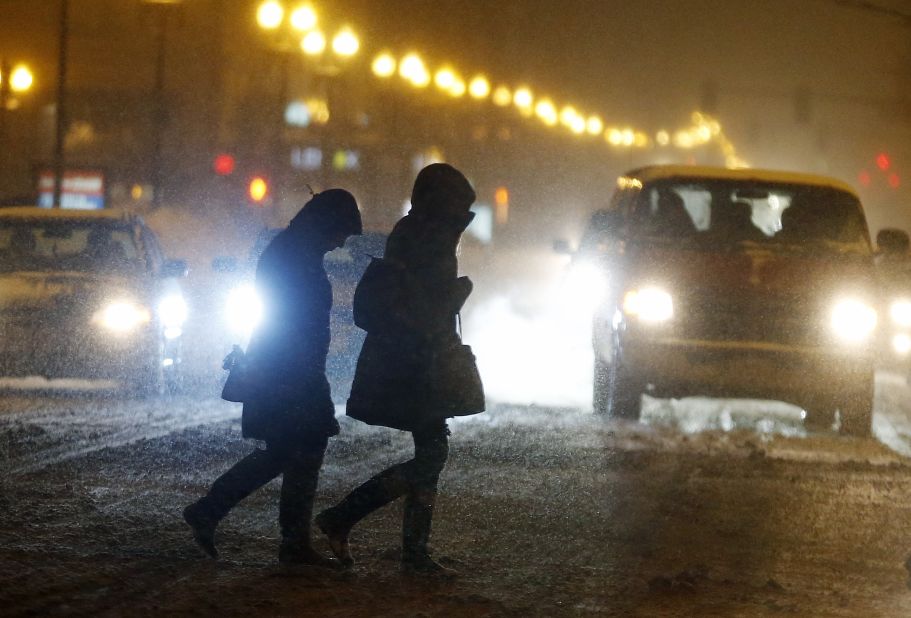 Pedestrians cross the street as snow falls in Boston on Saturday, February 14.
