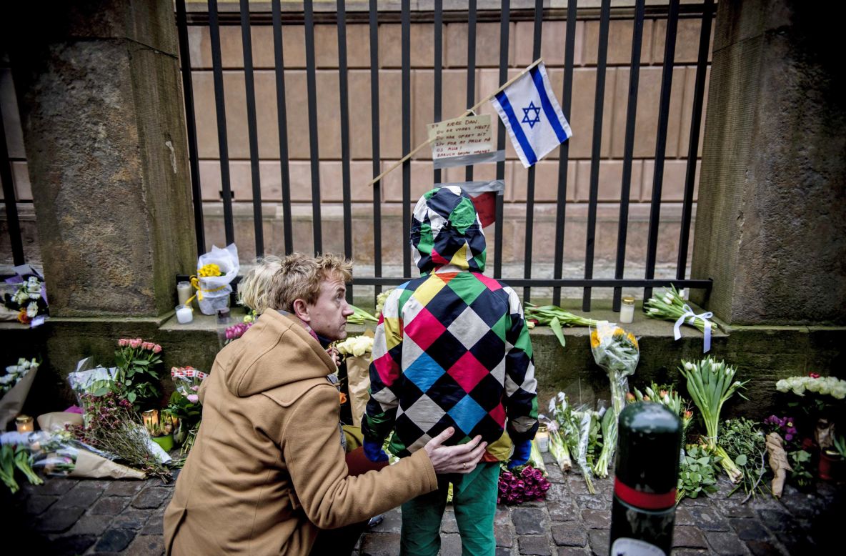 People look at a makeshift memorial on Sunday, February 15, outside a synagogue where an attack took place Saturday in Copenhagen, Denmark. Danish police shot and killed a man early Sunday suspected of carrying out shooting attacks at a free speech event and then at a Copenhagen synagogue.