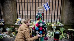 People stand by a makeshift memorial outside a synagogue where an attack took place in Copenhagen, Sunday, February 15. Danish police shot and killed a man early Sunday suspected of carrying out shooting attacks at a free speech event and then at a Copenhagen synagogue.