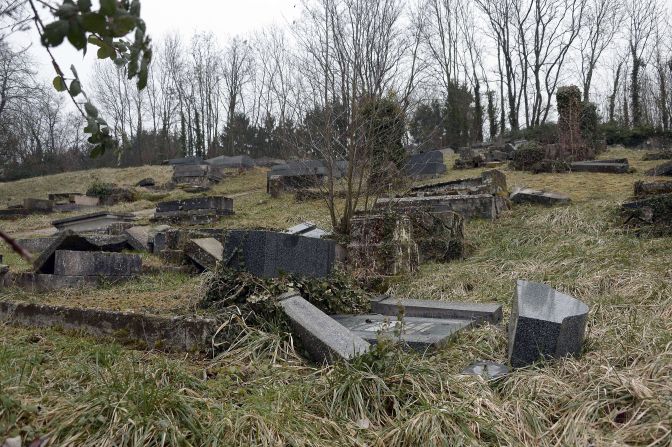 Several gray stone and glossy marble headstones are seen lying on the ground as if they had been toppled over.